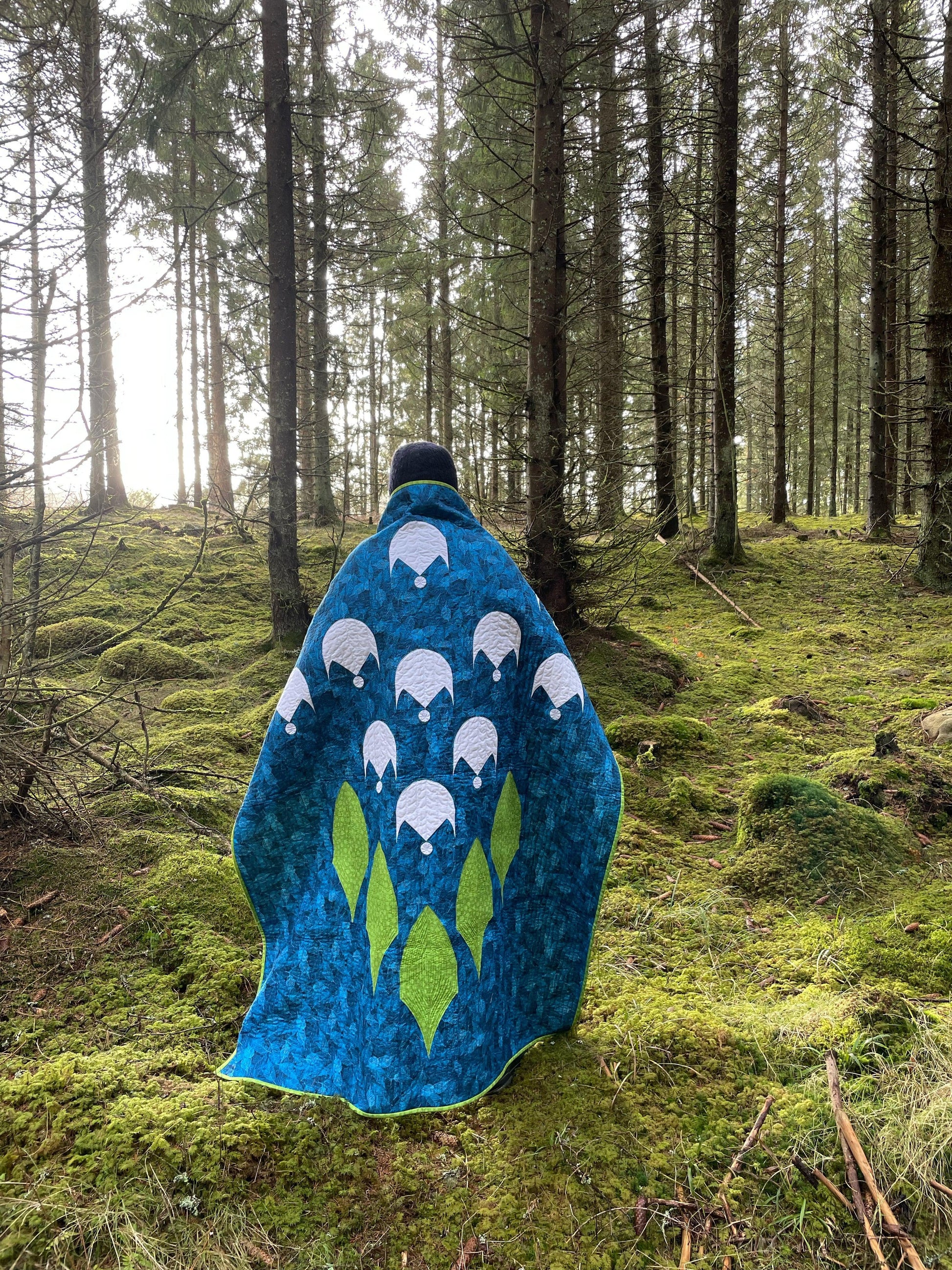 Person wearing quilt in the woods.